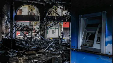 AFP People inspect a fire-damaged bank in the Lebanese city of Tripoli on 28 April 2020