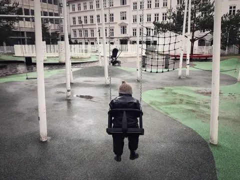 Peter Hove Olesen / Unicef A child sits on the swings in an empty playground