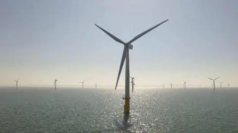 Lots of wind turbines in the sea, with one turbine up close at the front of the picture, and others in the background.