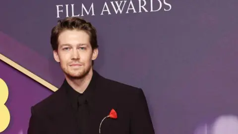 Getty Images Joe Alwyn with a single red flower on his dark suit