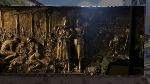 BCC A bronze memorial showing soldiers helping people. Gas masks are included in the design/ 