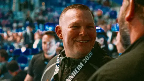 A smiley man in a crowd looks just right of the camera