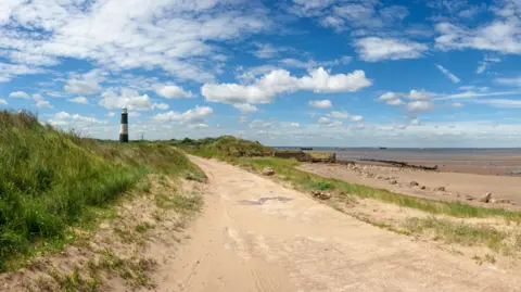 Abzee (via Getty Images) The remains of a road on a peninsula, flanked by sand dunes and sea.