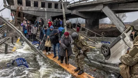 ROMAN PILIPEY/EPA A view of Ukrainian armed forces helping townsfolk escape from their village near Kyiv, crossing a wooden beam.