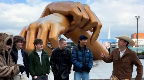 The band by a Psy statue in Seoul