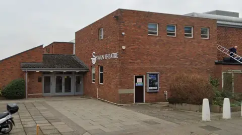 The entrance to The Swan Theatre, a brick building with a white image of a swan and "Swan Theatre" in white letters on one of the walls.