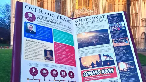 Kayleigh Cutforth A large red book with information on both sides, placed on the grass with the Cathedral building in the background.