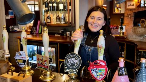Landlady pouring a pint of beer behind the bar of her country pub.