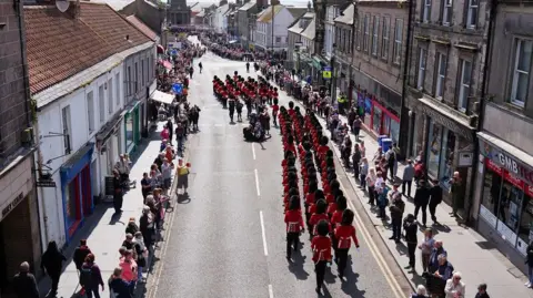 PA Media An aerial photo of the guards marching through Berwick. They are marching down the middle of a road lined with people and stone buildings.
