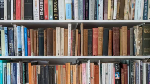 White shelves are stacked with books, some old, some new. 