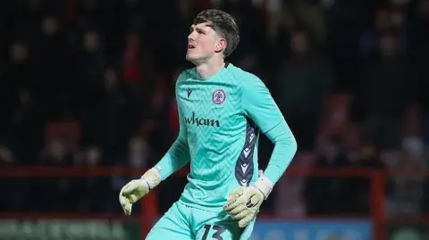 Ollie Wright on the pitch with his arms by his side, wearing Accrington kit, during a match