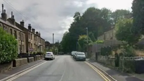 Google A residential street with terraced houses, parked cars and double yellow lines on both sides of the road. 