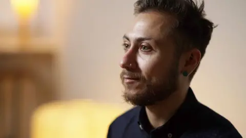 A close-up of Stephan Kyriacou, who has brown hair, a beard and a nose ring, and is wearing a navy shirt