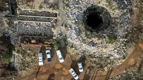 AP Aerial view of one of the mine shafts of the Stilfontein mine in South Africa, with police vehicles parked nearby.