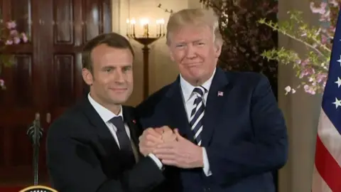 Trump and Macron hold hands.