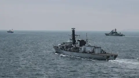 Image shows three ships out at sea, the one in the middle is Royal Navy vessel HMS Somerset