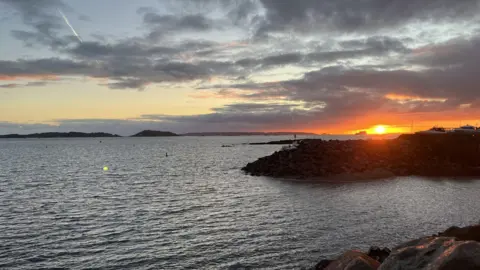 BBC An east coast sunrise over the sea on Guernsey. The sea is calm and the sunrise is to the right of the image.