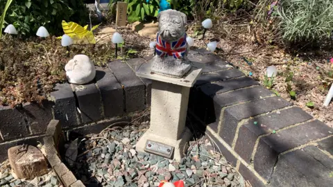 Shariqua Ahmed/BBC A bulldog statue with a British flag painted on him, placed in a small stoned- enclosure. 
