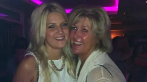 Family Two women smiling with blonde hair they are both wearing white outfits. They are both looking into the camera. 