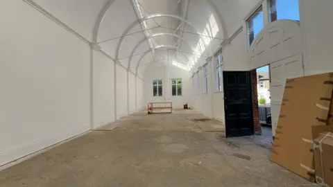 Tom Jackson/BBC An empty Mill Road library building. It has its walls painted white, with a few cardboard boxes lying to the side of the room. The dark door is open to the outside.