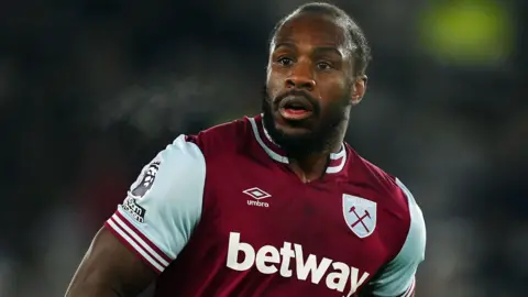 PA Media A close-up of a footballer with dark hear and beard in a maroon and sky blue West Ham kit as he runs on a pitch in the middle of a game. He is sweating.