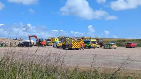 Emergency service vehicles, including ambulances and fire engines, in a car park at Weybourne Beach in Sheringham.