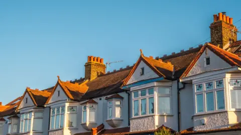The top floor and roofs of some terraced houses, beneath a blue sky