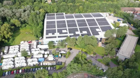 A view of The Bottle Yard Studios site from the air. It shows solar panels on the roof, trees, shrubbery and parked cars. 