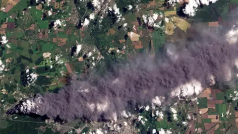 Planet Labs PBC/Reuters A satellite shows dark smoke coming from a small area and billowing out to cover a large area of countryside