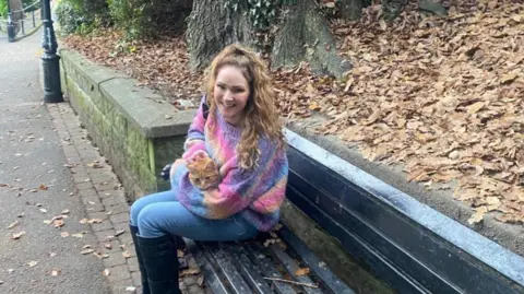 Verity Maybury-Griffiths Raymond the ginger tom cat sitting on the lap of a smiling woman in the park