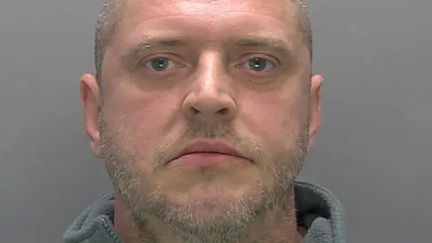 Paul Page is looking at the camera in a police custody photo. He is balding and has a stubbly beard and moustache.
