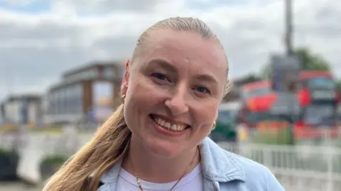 Jon Wright/BBC Mrs Hoian smiles at the camera while standing outside. She wears a light denim blue shirt that is open and a white T-shirt underneath.