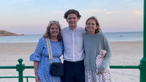 Emily Plane (right) with her mother and brother stand in front of a beach in Jersey