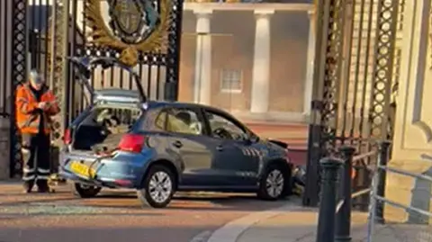 PA Media Screengrab from video of workman about to remove a car outside Buckingham Palace on Saturday. A man was arrested after crashing his vehicle into the gates of Buckingham Palace, London. Armed officers arrested the man at the scene on suspicion of criminal damage and he was taken to hospital, the Metropolitan Police said. Scotland Yard said his car "collided with the gates" of the royal residence at 2.30am on Saturday. Issue date: Sunday March 10, 2024.