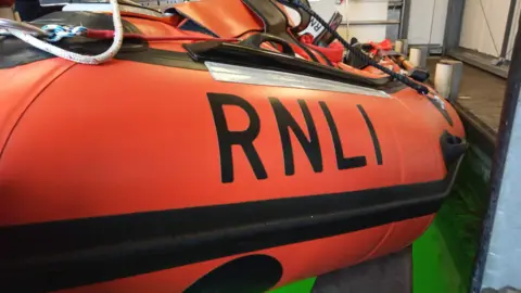 An orange lifeboat with RNLI written on the side in bold, black writing. 