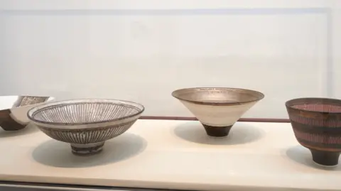 Jo Underhill Four light and dark brown ceramic bowls laid out on a cream surface. There are well lit and appear to be on display.
