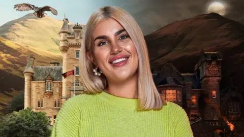 Livi Deane standing in front of the castle where The Traitors is filmed. An owl soars over the mountains in the background.