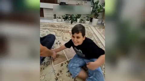 Boy smiling on carpet with a football tactics board in front of the football on TV