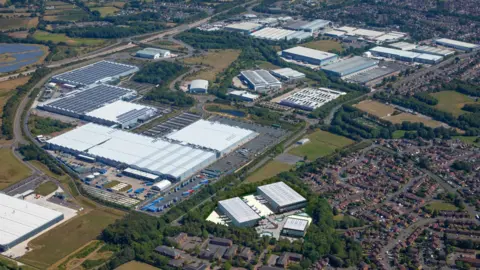 An overhead view of a vast industrial site, next to a housing estate, showing a view of several warehouses.
