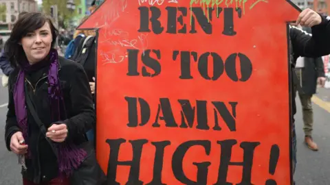 Getty Images A protester seen with 'The Rent Is Too Damn High!' sign during a protest against the housing crisis 'Raise the Roof'; On Saturday, May 18, 2019, in Dublin, Ireland.