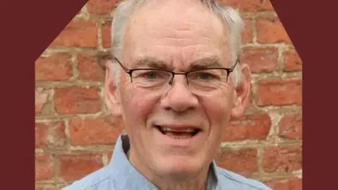 Restore A man with glasses and white hair. A brick wall is behind him. 