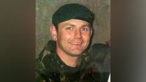 Dave Pettifer An old photo of a man in a military jacket and green beret, smiling at the camera.