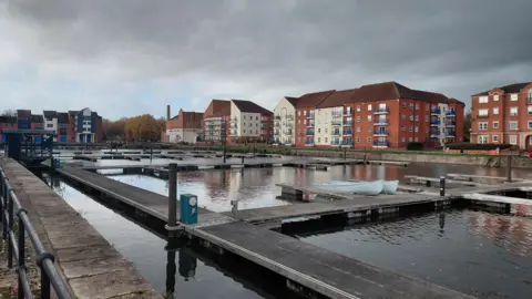 Daniel Mumby Residential buildings around docks filled with water are pictured on a grey day. 