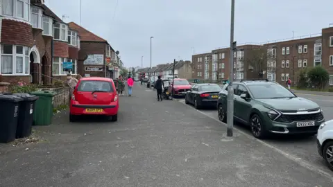 George Carden / BBC Whitehawk Road with shops on one side and flats on the other. The pavement is about 15ft wide.