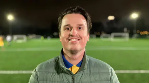 Football player, Jake Majthenyi, looks into the camera while other men play football behind him