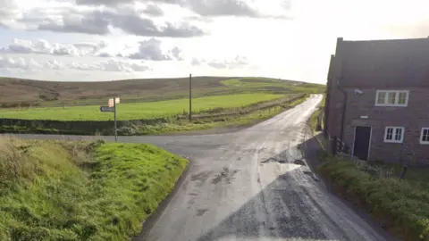 Google A country road leading to a junction, with a cottage to the left. Acres of hills and green farmland can be seen ahead