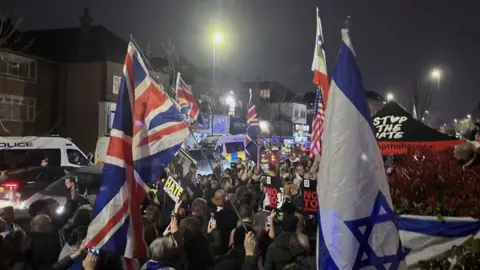 PA Media Protest group Our Fight UK stage a 'rally against Jew hate' near the scene in Highfield Road, Golders Green, London, after an arson attack. Israeli and UK flags can be seen waving 