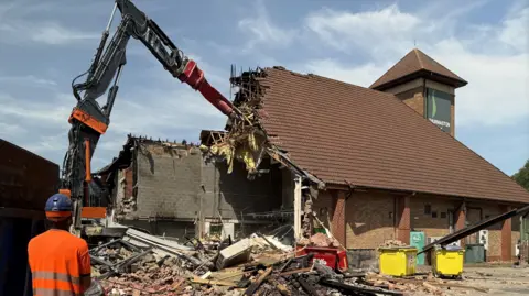 a high-reach excavator tears down a building made of brick