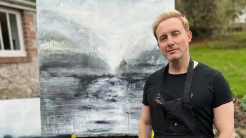 Tom Hope PR Ian in front of one of his paintings