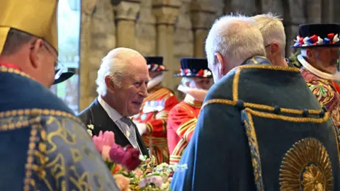 PA Media King Charles, smiling, while talking to men in ceremonial clothing ahead of the service at Durham Cathedral.